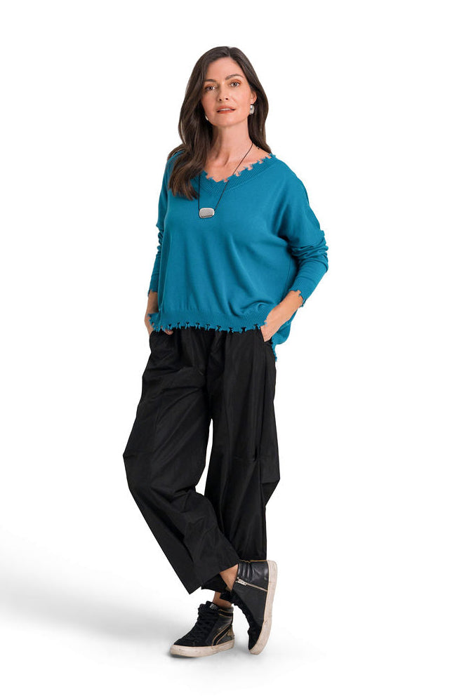 A woman modeling a galaxy teal long-sleeve pima cotton v-neck knit top and black wide-leg pants against a plain white background.
