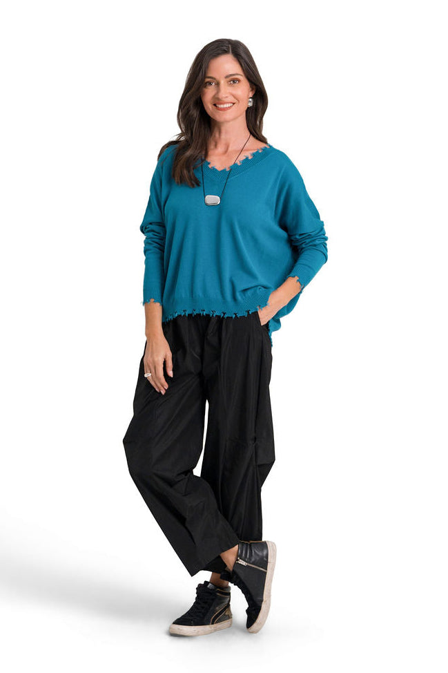 A woman modeling a galaxy teal long-sleeve pima cotton sweater and black wide-leg pants against a plain white background.