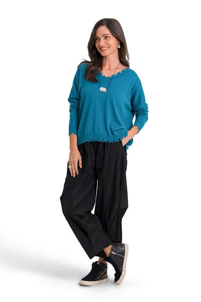 A woman modeling a galaxy teal long-sleeve pima cotton cv-neck sweater and black wide-leg pants against a plain white studio background.