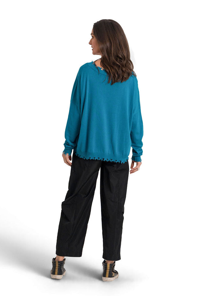 A woman shown from the back wearing a galaxy teal long-sleeve pima cotton v-neck sweater and black pants, standing against a plain white studio background.