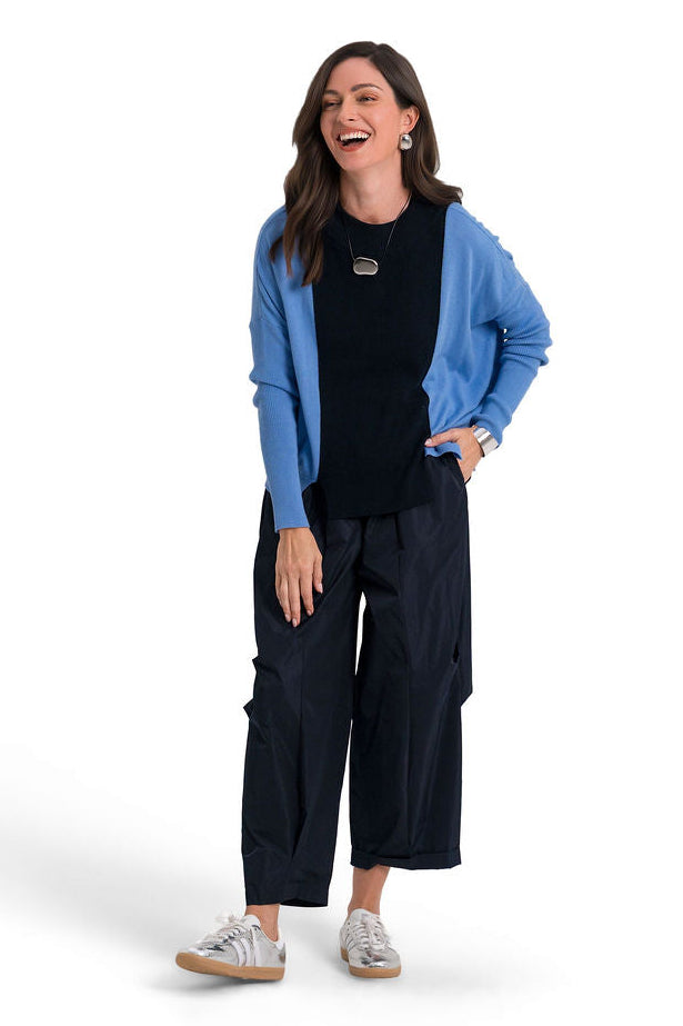 A woman modeling a two-tone pima cotton sweater with a blue body and dark navy sleeves, worn over navy wide-leg pants, on a white studio background.
