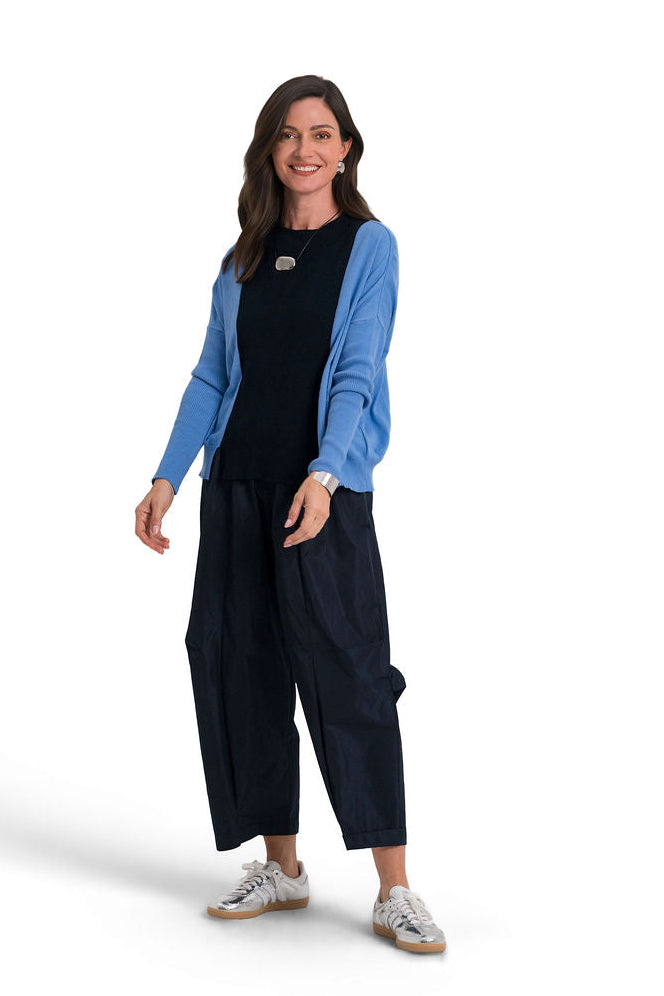 A woman modeling a with a light blue and navy blue long-sleeve pima cotton sweatshirt and silver sneakers against a plain white background.