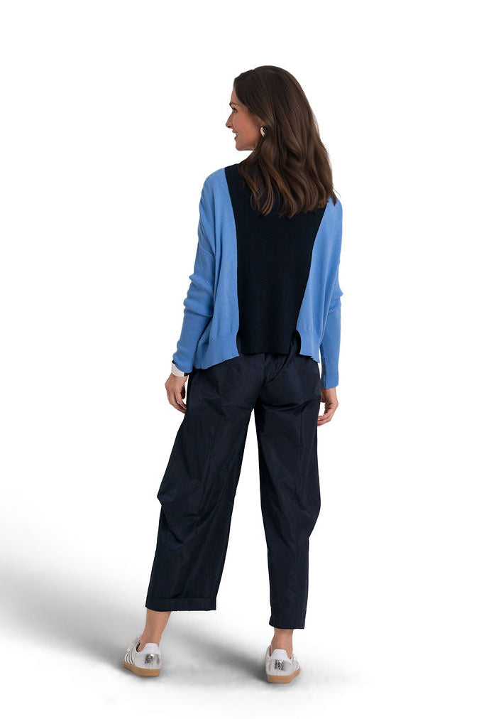 A woman is shown from the back wearing a light blue pima cotton sweater, paired with dark navy wide-leg nylon cargo pants and silver sneakers, set against a plain white studio background.