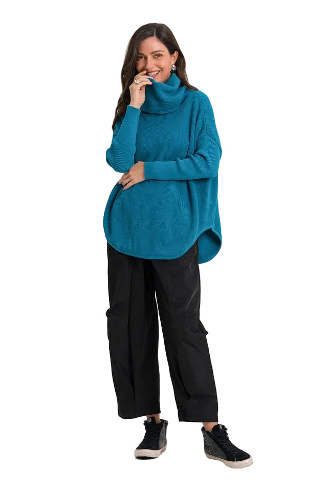 A woman modeling a teal blue pima cotton turtleneck sweater, black wide-leg cargo pants, and black sneakers against a plain white background.
