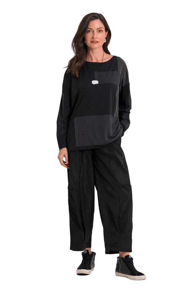 A woman modeling a 100% pima cotton black long-sleeve top with a tonal chest panel and black wide-leg pants, standing against a plain white studio background.