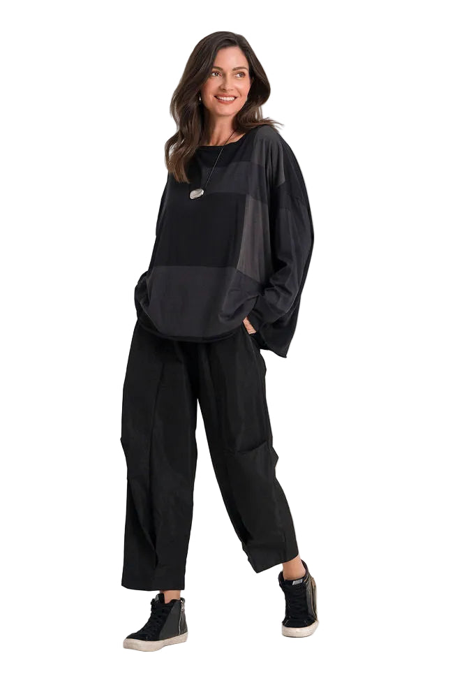 A woman modeling a 100% pima cotton black long-sleeve top with sheer side panels and black wide-leg pants, standing against a plain white studio background.