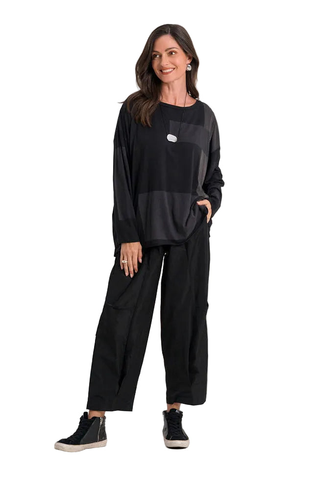 A woman modeling a 100% pima cotton black long-sleeve top with a small white chest logo and black wide-leg pants, standing against a plain white studio background.