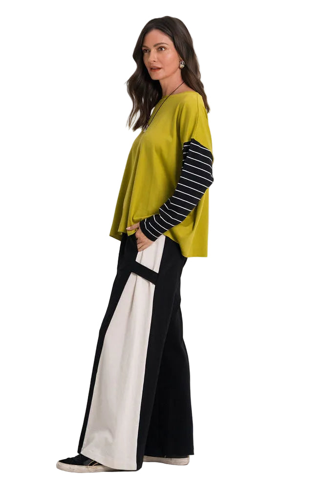 A woman modeling a two-piece outfit consisting of a cropped olive green top with black and white striped sleeves, paired with 100% cotton wide-leg colorblock pants in black, white, and green, against a plain white studio background.