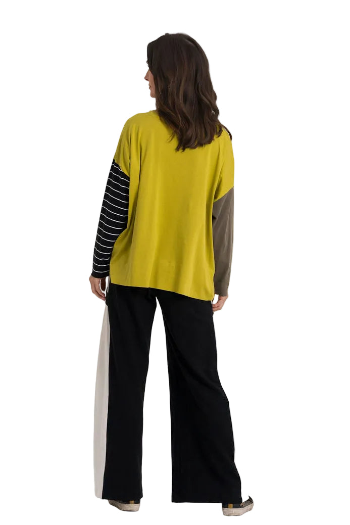 A model viewed from behind wearing a color-blocked long-sleeve top with a yellow body, black and white striped sleeves, and gray back panels, paired with 100% cotton black wide-leg pants.