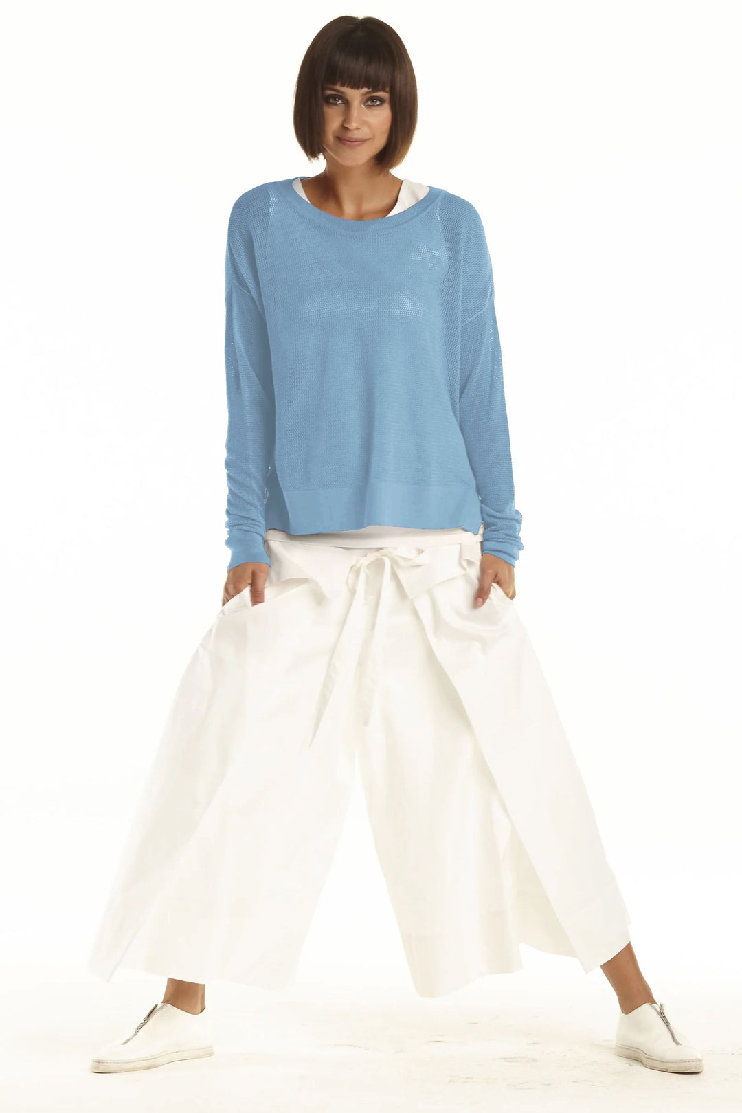 Woman wearing a blue top and white pants on a white background