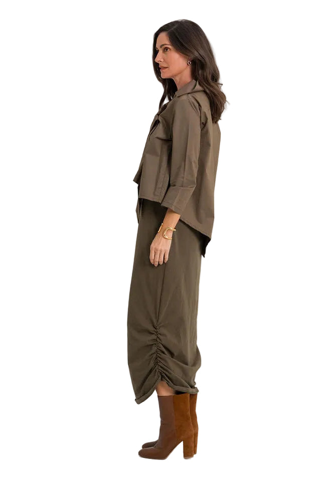 A woman shown in side profile wearing an 100% cotton olive green two-piece outfit consisting of a cropped long-sleeve top and matching gathered wide-leg pants, paired with brown ankle boots, against a plain white studio background.