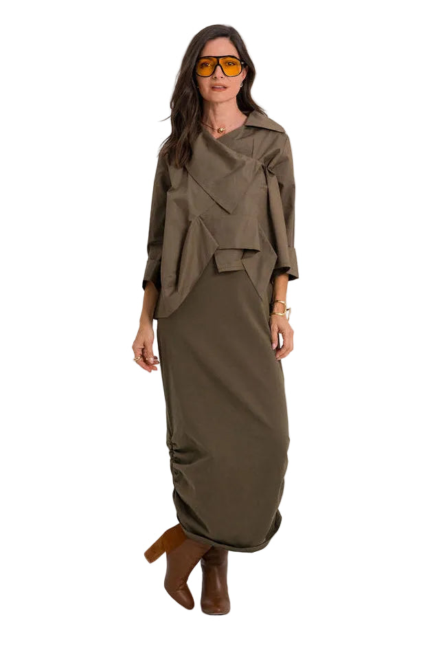 A woman modeling a draped, 100% cotton wrap-style midi dress in an olive brown color, styled with yellow-tinted sunglasses and brown ankle boots against a plain white studio background.