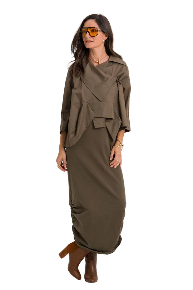 A woman modeling a matching two-piece outfit consisting of an 100% cotton olive green draped long-sleeve top and a matching pleated maxi skirt, styled with brown leather ankle boots and yellow-tinted sunglasses against a plain white studio background.
