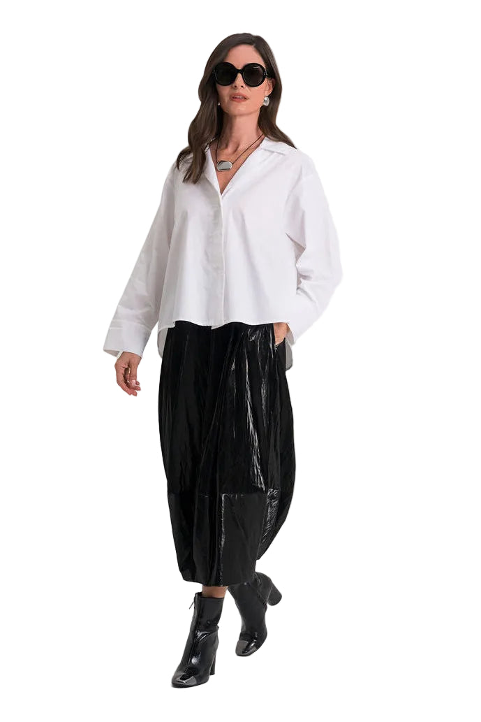 A woman modeling a 100% cotton white long-sleeve button-up shirt and black wide-leg pleated trousers with black ankle boots, photographed against a seamless white studio background.