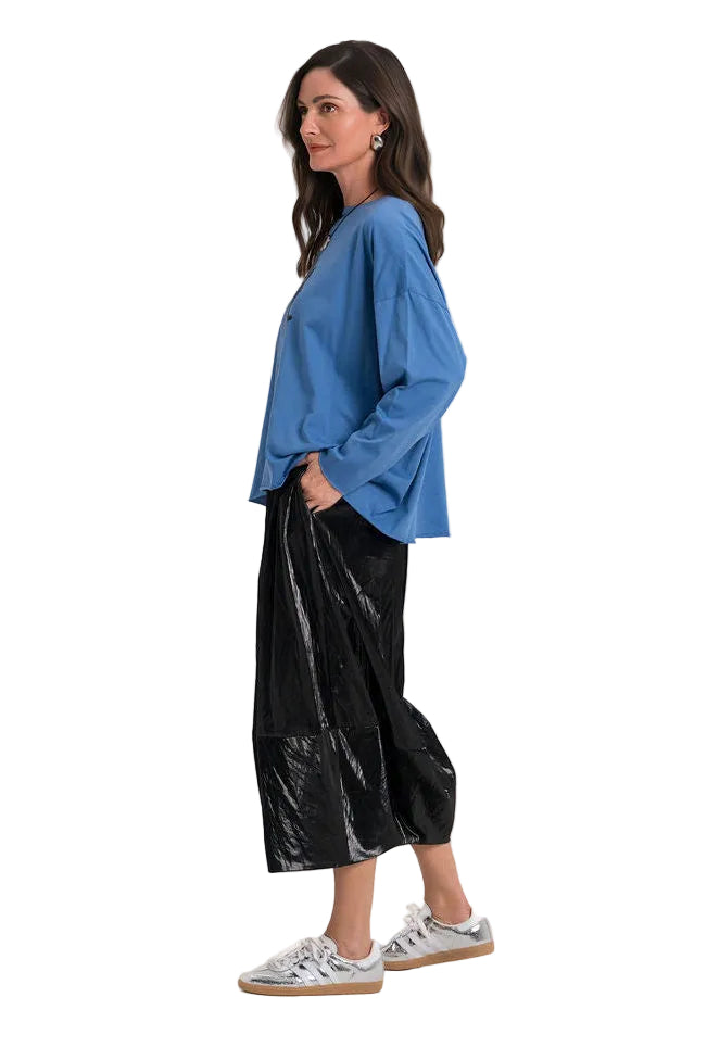 A woman modeling a blue long-sleeve top and shiny black wide-leg pants against a plain light gray studio background.