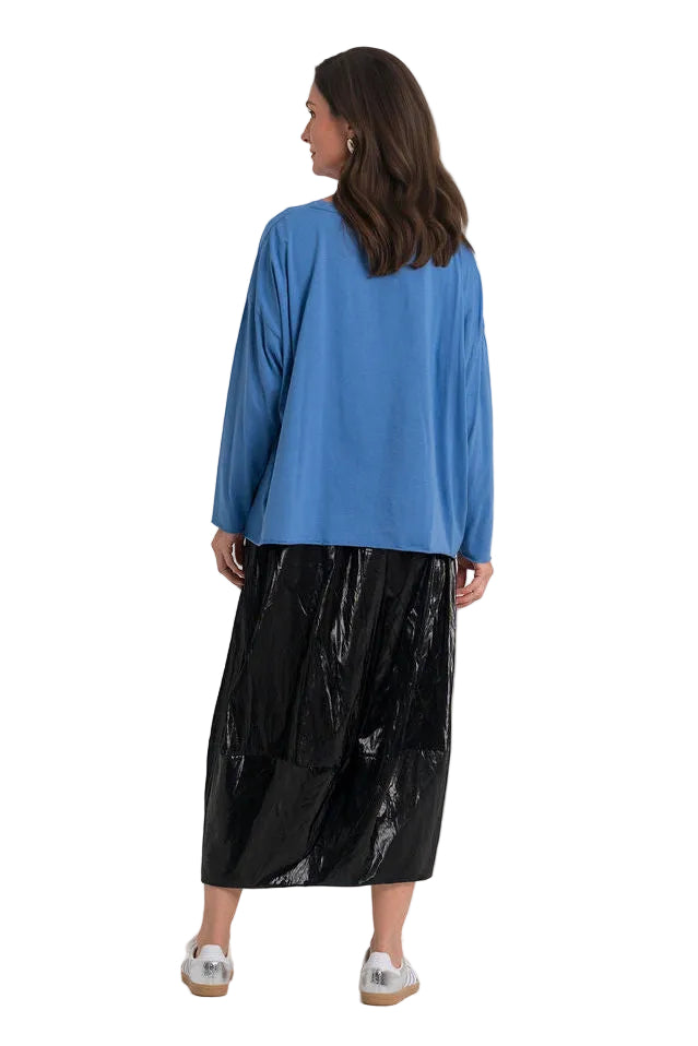 A woman is shown from behind wearing a 100% pima cotton blue long-sleeve top and a shiny black midi skirt, standing against a plain white studio background.
