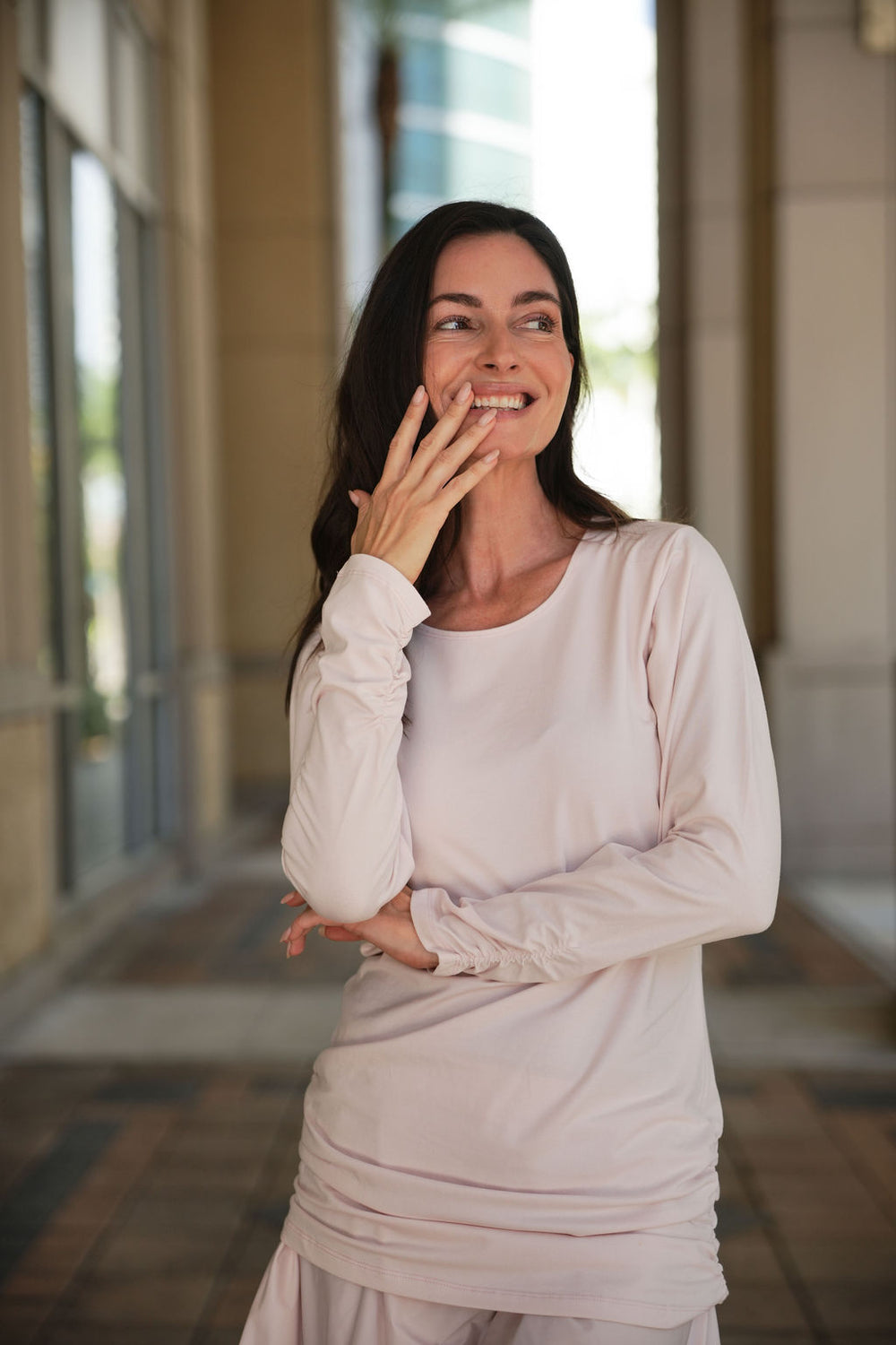 Woman in a light-colored blush lycra ruche shirt standing in a sunlit hallway