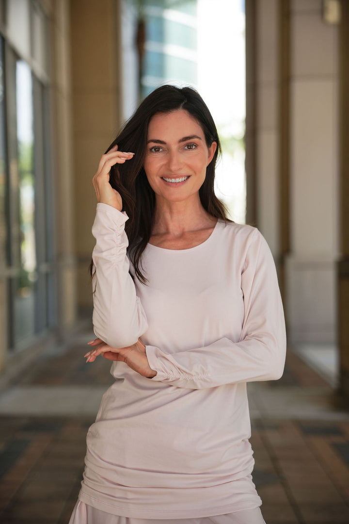 Woman in a light-colored blush crewneck top standing in a well-lit outdoor setting in Fort Lauderdale
