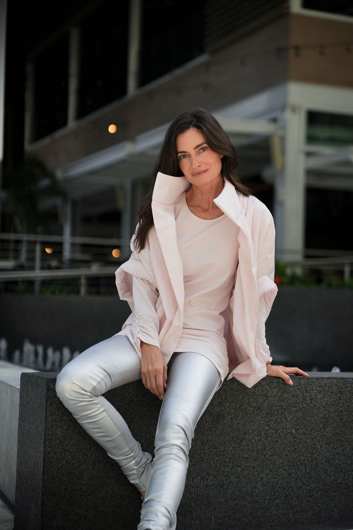 Woman sitting on a ledge wearing a light pink blush chic cape outfit with a blurred background