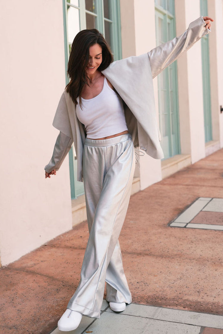 Woman in light gray vegan leather outfit standing on a sunlit walkway with columns in coral gables.