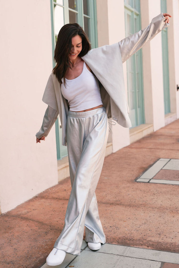 Woman in light gray vegan leather outfit standing on a sunlit walkway with columns in coral gables.