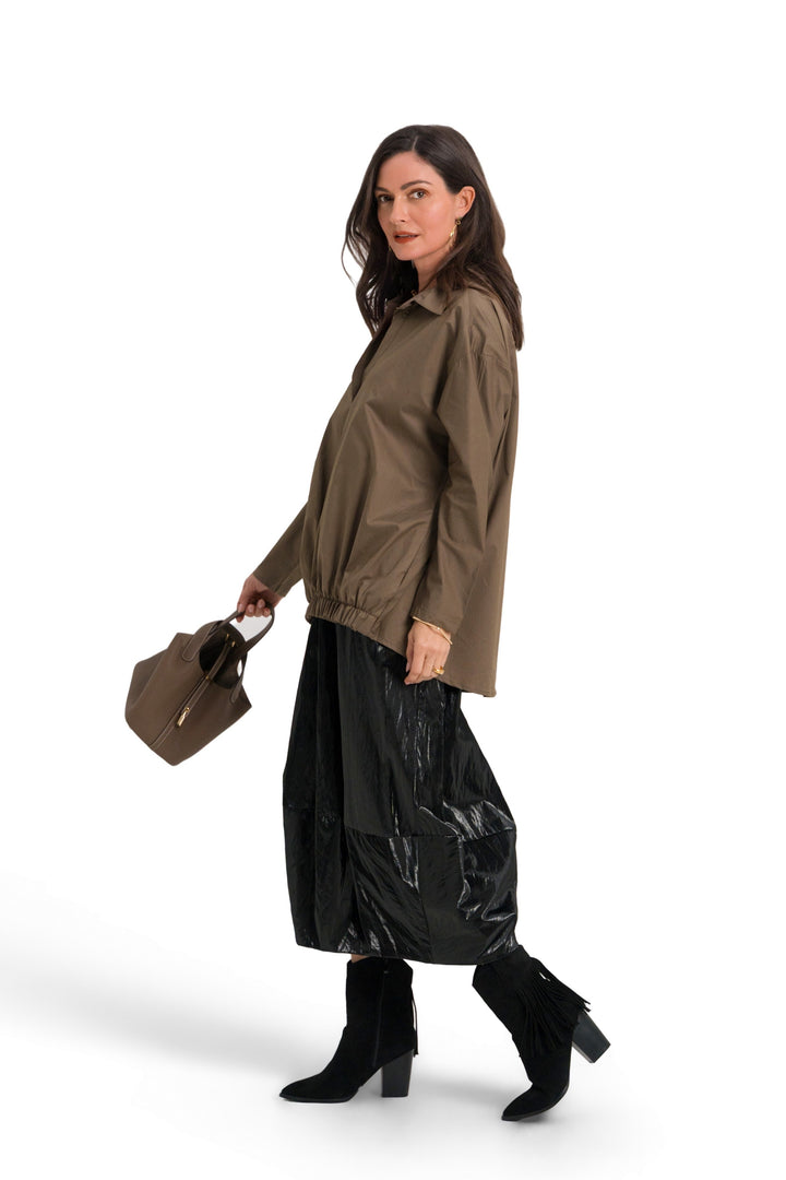 A woman modeling an 100% cotton olive green hooded jacket, black wide-leg pants, and black boots, holding a brown handbag against a solid white background.