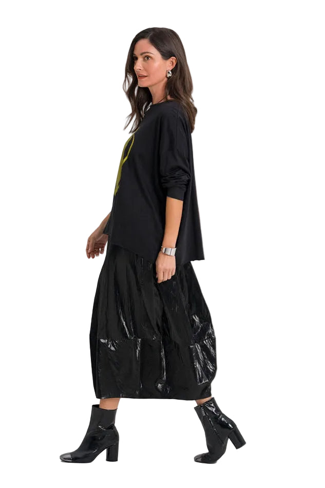 A woman modeling a 100% pima cotton black long-sleeve top and a black pleated midi skirt with a glossy finish, paired with black ankle boots, against a plain white studio background.