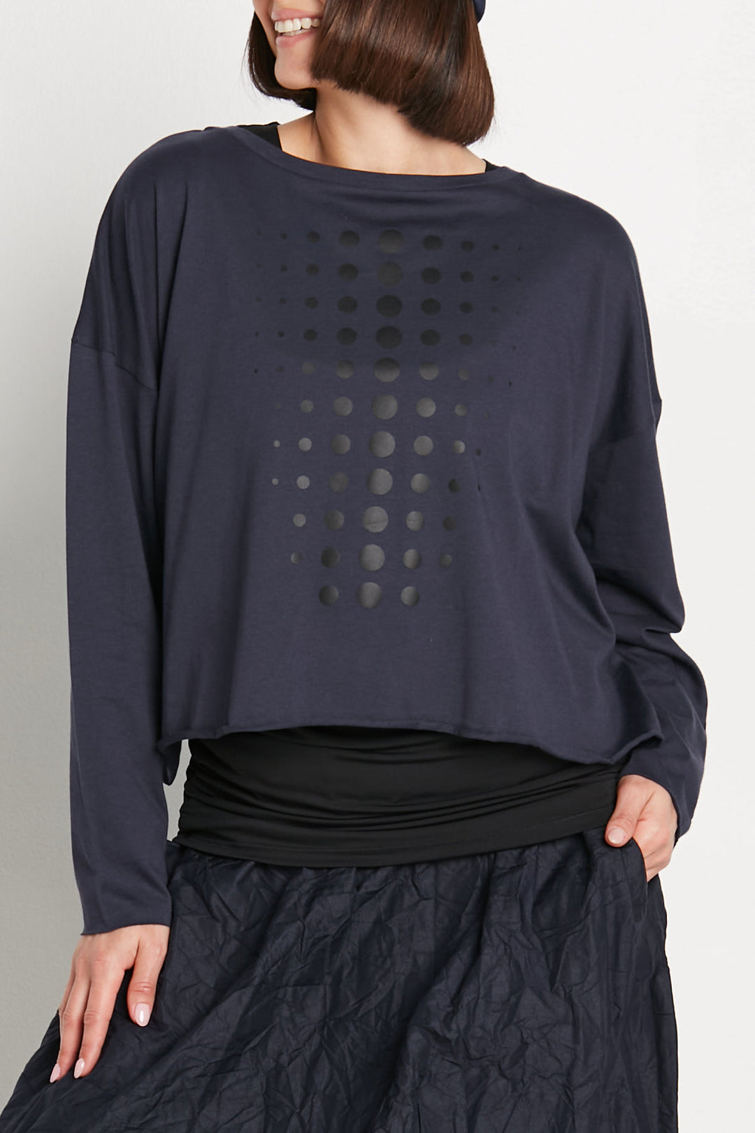 Person wearing a dark blue long-sleeve top with a patterned design on a plain background