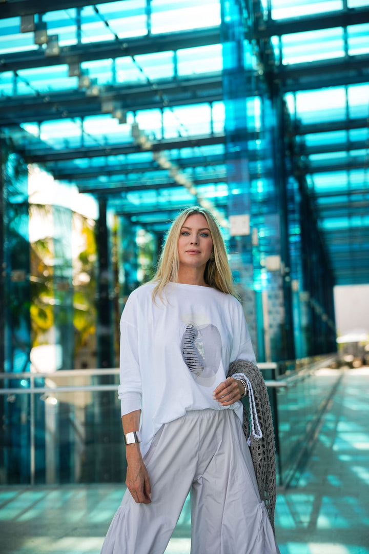 Woman in a white pima cotton boxy t-shirt standing in a modern building with glass walls.