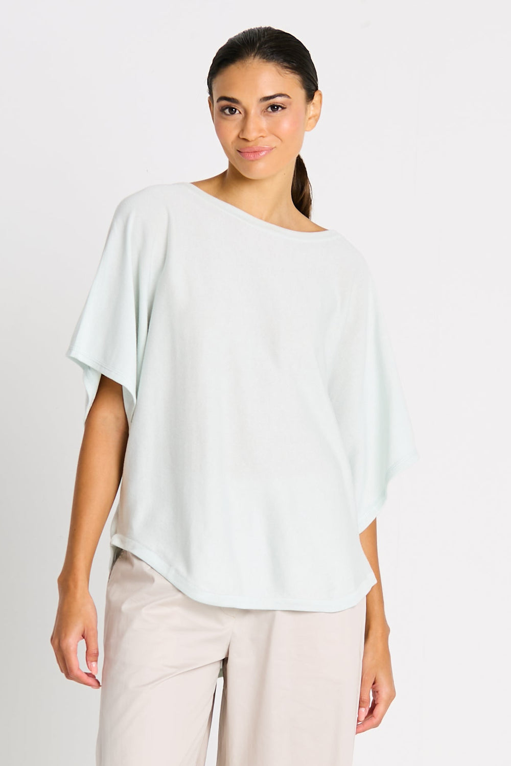 Woman wearing a light green top and beige pants on a white background