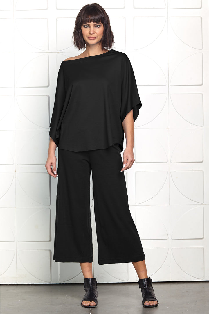 Woman wearing a black outfit against a white tiled wall.