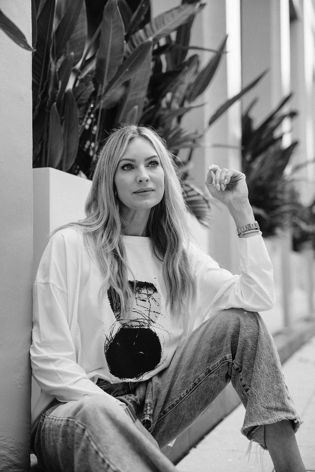 Black and white photo of a woman sitting outdoors with plants in the background wearing a white pima cotton shirt.