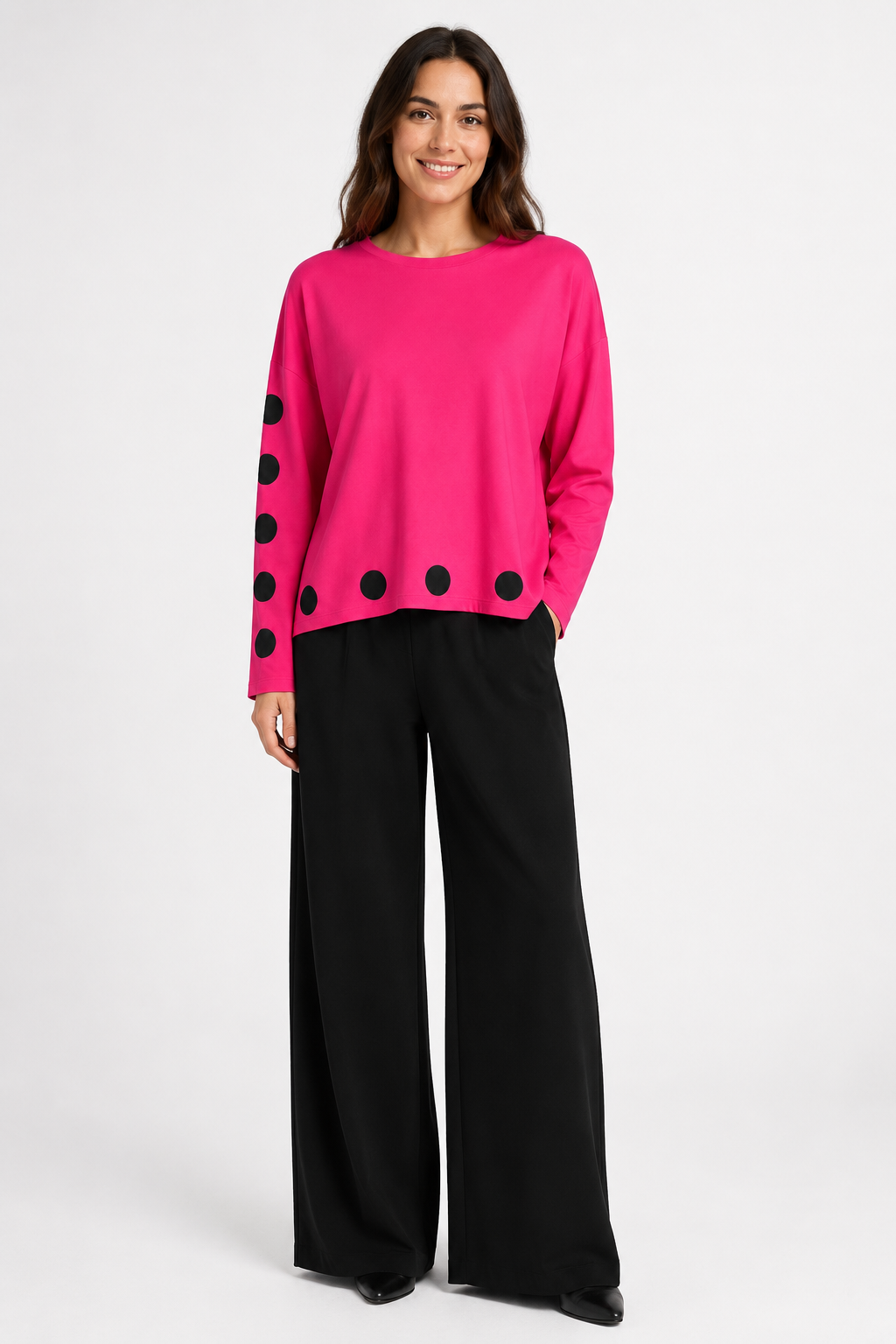 Woman wearing a bright pink pima cotton shirt with black polka dots and black wide-leg pants on a white background