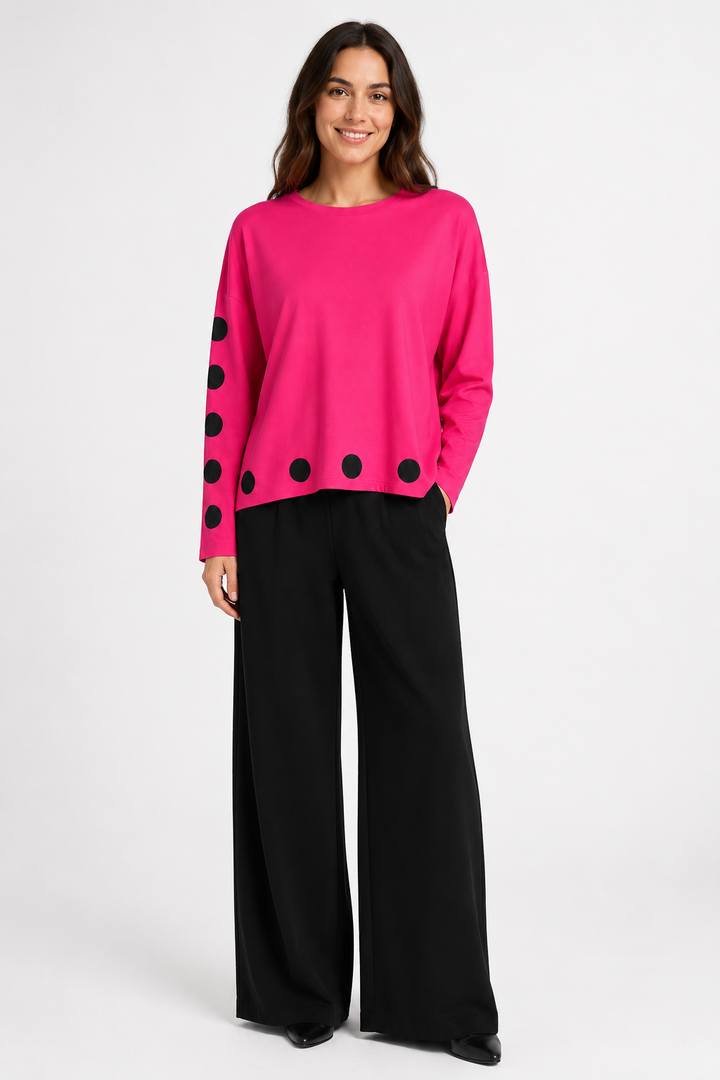 Woman wearing a bright pink pima cotton shirt with black polka dots and black wide-leg pants on a white background