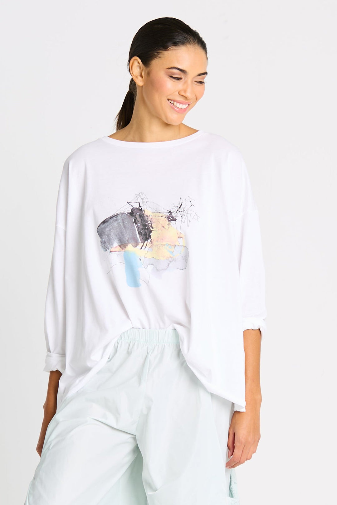 Woman wearing a white oversized pima cotton shirt with a watercolor graphic design on a plain background