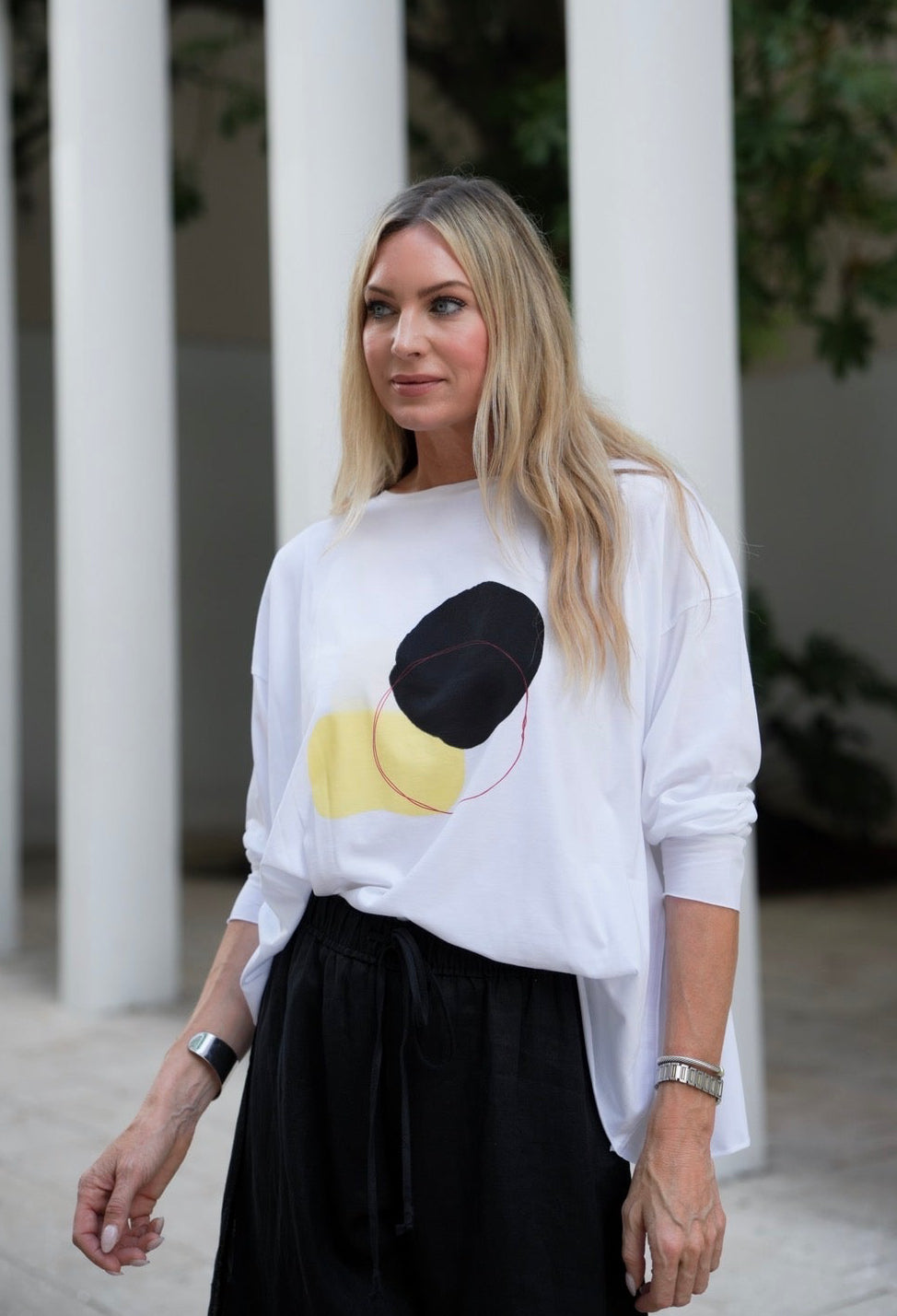Woman wearing a white Pima cotton shirt with black and yellow abstract design outdoors.