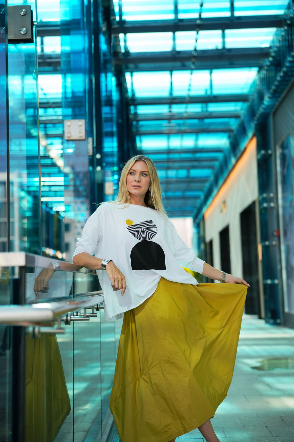 Woman in a modern building wearing a pima cotton white top with a black and gray design and a yellow skirt.