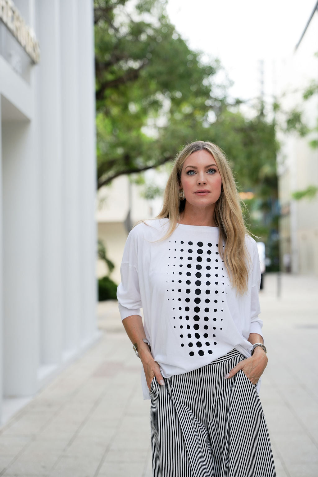 Woman wearing a white pima cotton shirt with black dot pattern and striped pants on a city street.