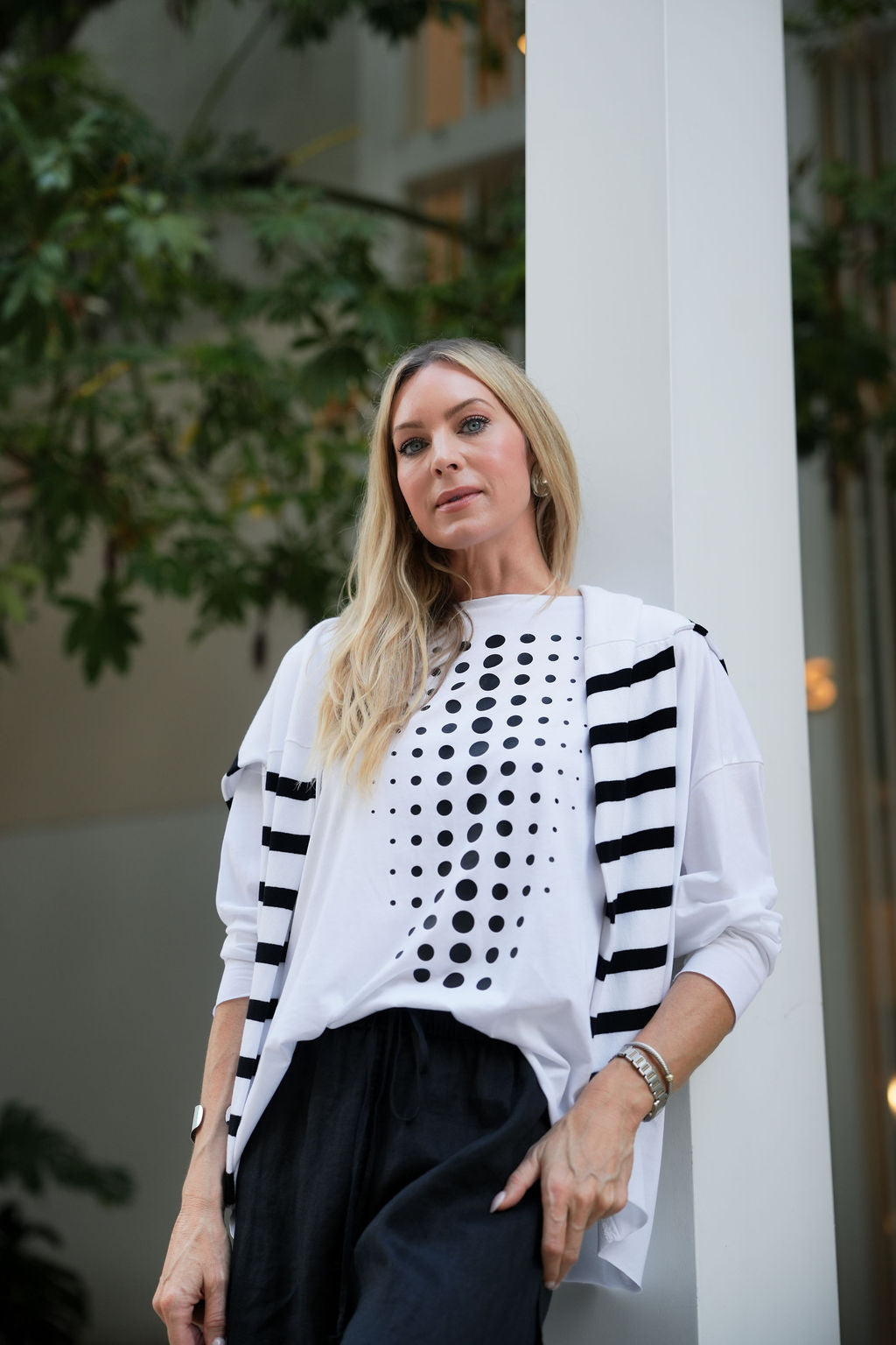 Woman wearing a white pima cotton top with black patterns and a black skirt, standing outdoors.