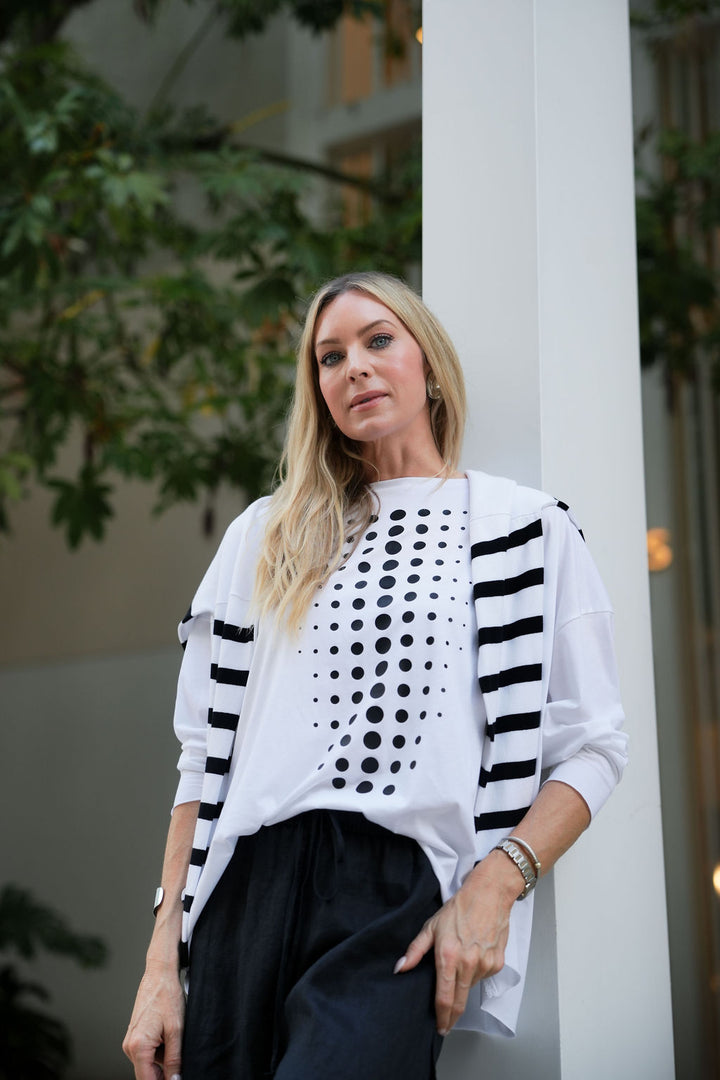 Woman wearing a white pima cotton top with black patterns and a black skirt, standing outdoors.