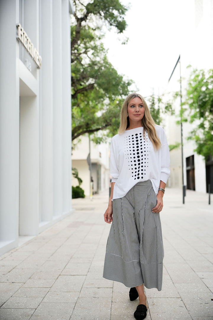 Woman wearing a white pima cotton shirt with a black geometric pattern and gray striped pants on a city street.