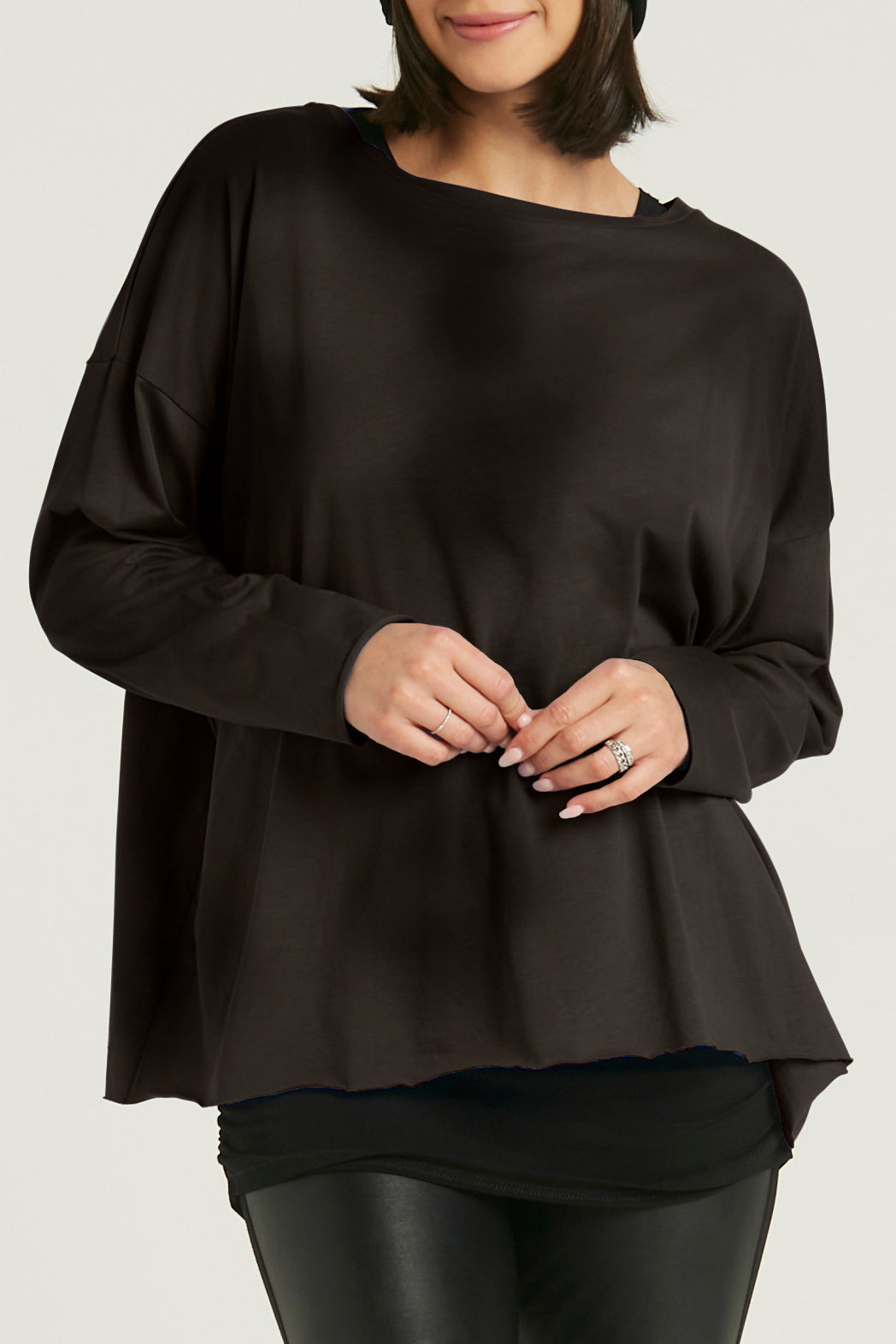 A person wearing a black boxy tee with long sleeves, paired with black leggings and black boots. Accessories include a black hat and sunglasses.