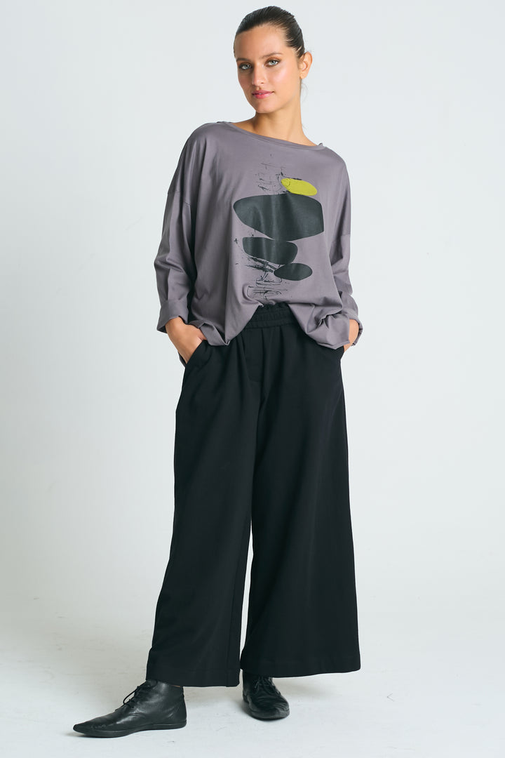 A female model wearing a gray Pima cotton boxy tee with an abstract graphic and wide neckline, paired with black pants.