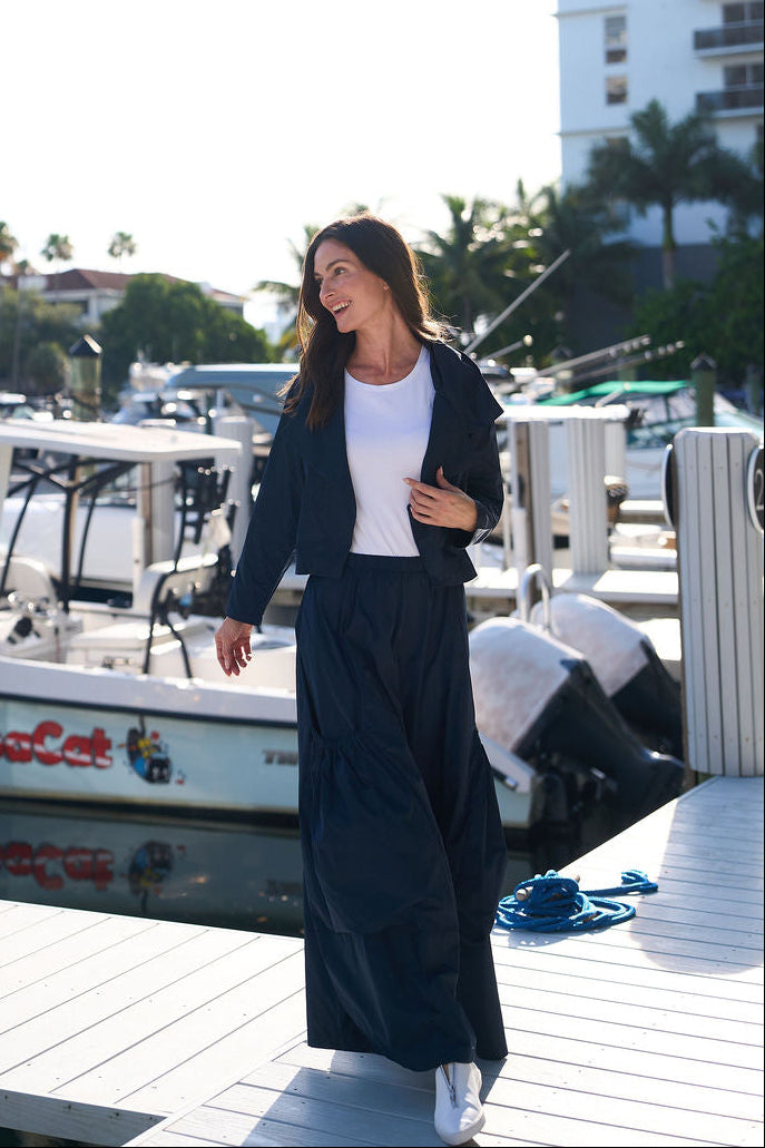 Woman in a midnight blue outfit standing on a dock with boats and buildings in the background