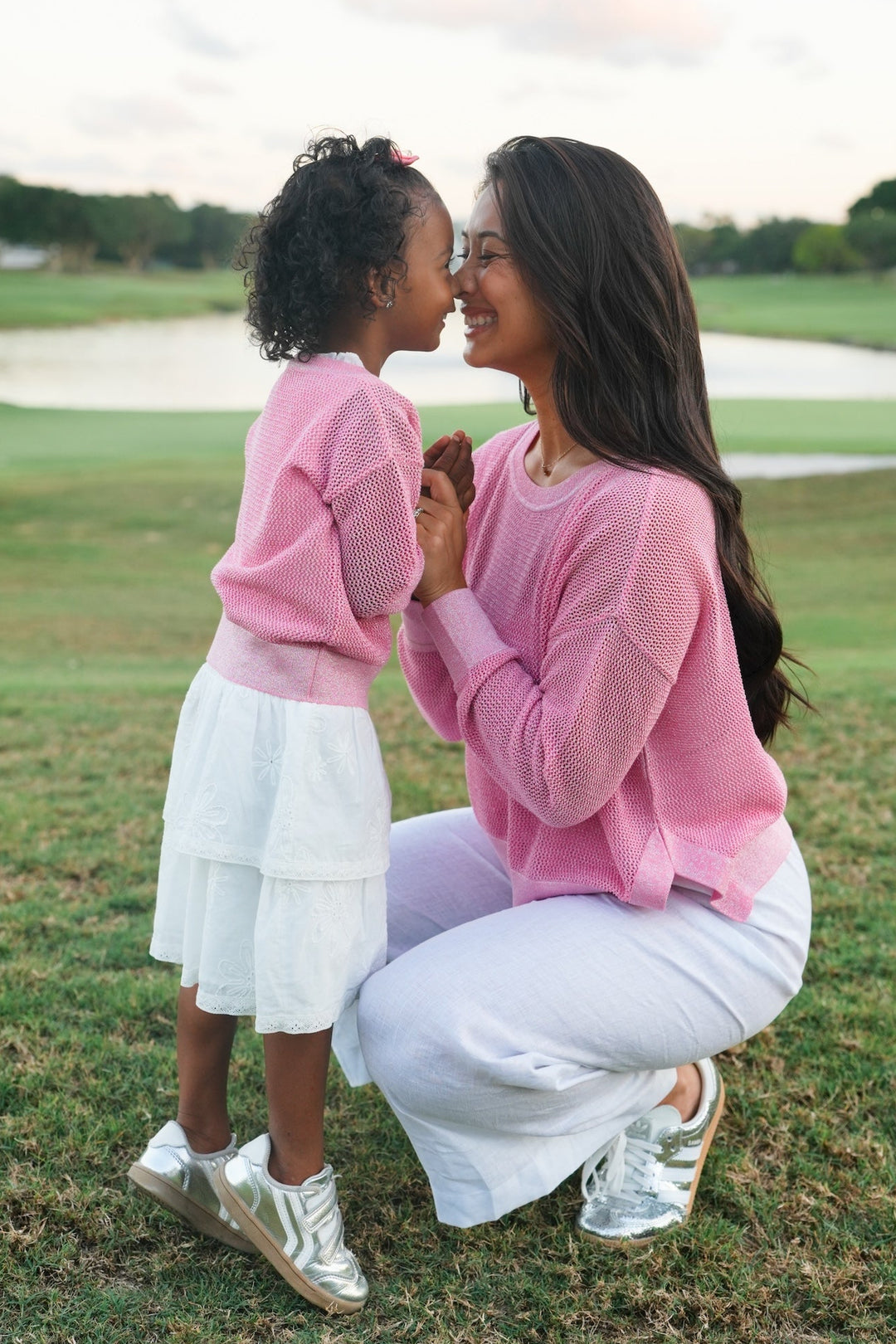 Woman and child in pink shirts and white pants on a grassy field