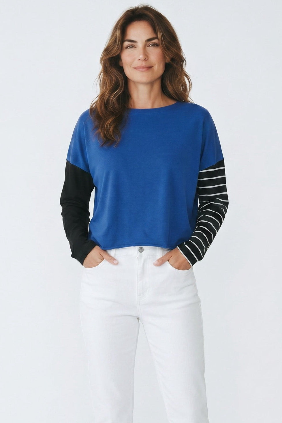 Woman wearing a blue and black long-sleeve top with white pants on a light gray background
