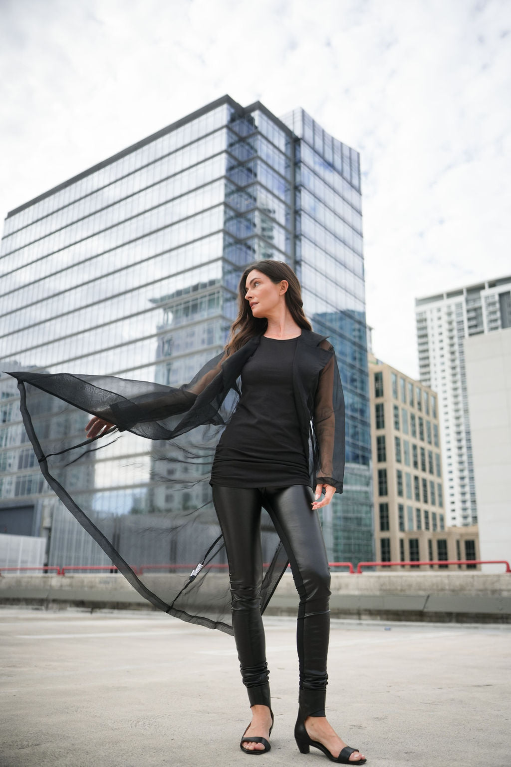 Woman in black organza trench coat with black vegan leggings against a cityscape background