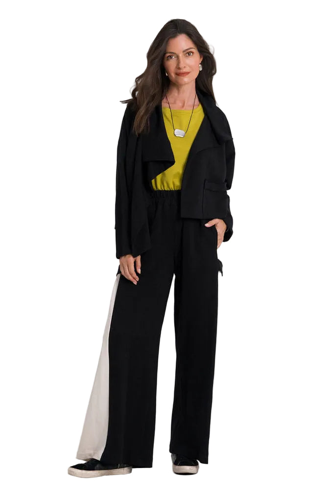 A woman modeling a black tailored outfit consisting of a cropped blazer, black 100% cotton wide-leg trousers, and a bright yellow top, standing against a plain white studio background.
