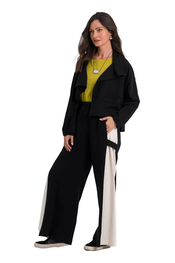 A woman modeling a 100% cotton black wide-leg pants set with contrasting white side panels, styled with a yellow-green top and a black jacket, against a plain white studio background.